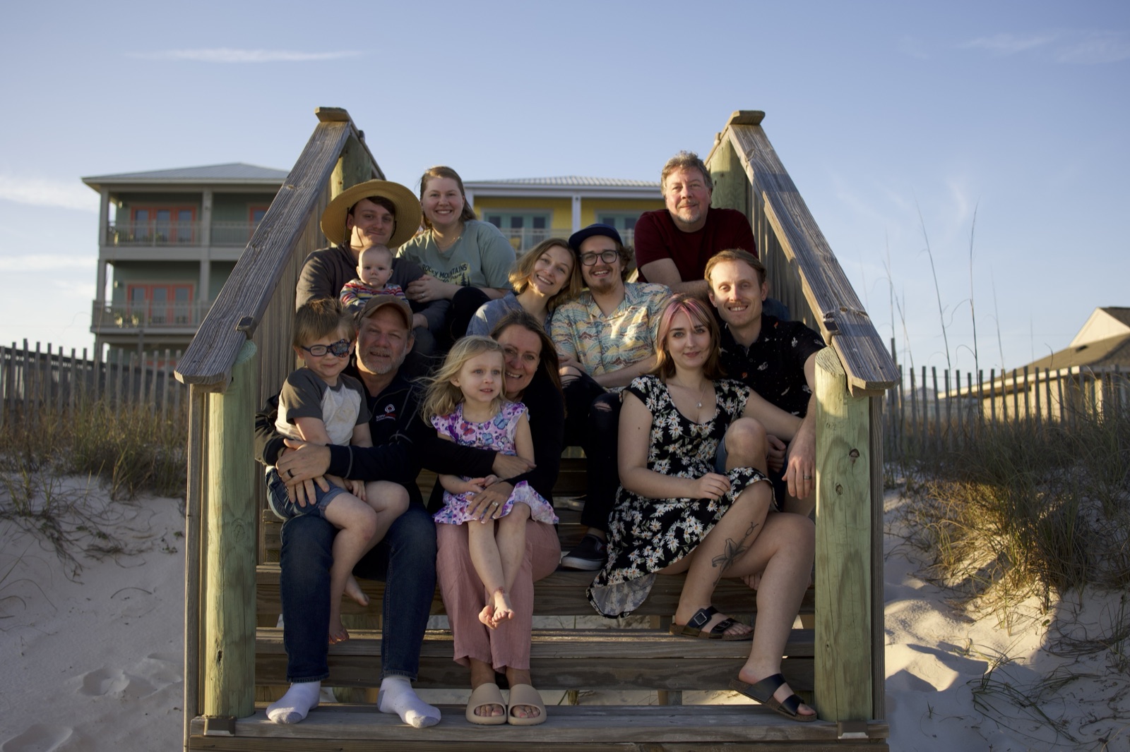 The family behind Gulf Shores Beach Life gathered on the boardwalk steps at golden hour, beach houses behind them
